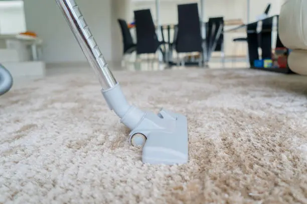 Close up of a vacuum cleaner being used while removing dirt on white carpet