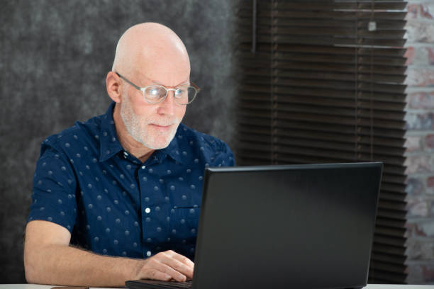 istock mature man with a white beard and blue shirt using a laptop 1131997586