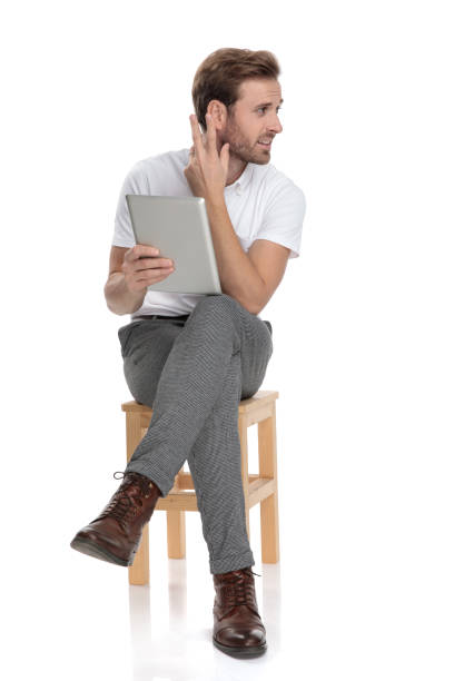 istock confused and curious man sitting, holds a tablet and gestures 1131999438