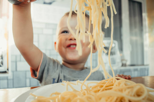 chéri dans la cuisine mangeant avec impatience des pâtes - child eating pasta spaghetti photos et images de collection