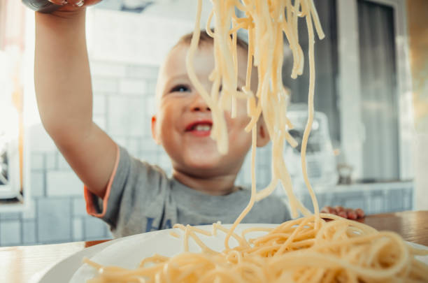 Baby in the kitchen eagerly eating pasta Baby in the kitchen eagerly eating pasta with a fork and hands, very neat kids eating noodles stock pictures, royalty-free photos & images