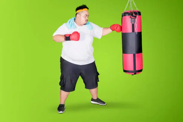 Image of overweight man punching a boxing bag and exercising in the studio with green screen background
