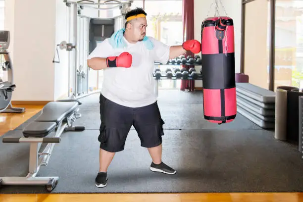 Image of overweight man punching a boxing bag and exercising in the gym center