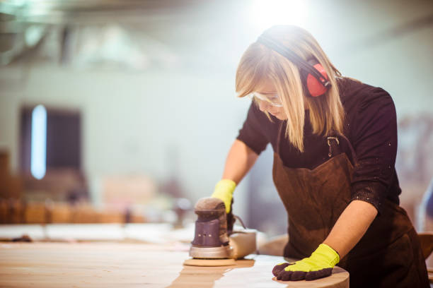 istock Girl carpenter using an orbit sander to sand down a wooden panel on a work bench in a workshop 1132001668