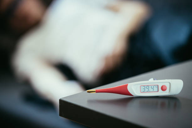 Fever thermometer in the foreground, ill man lying on the sofa in the blurry background