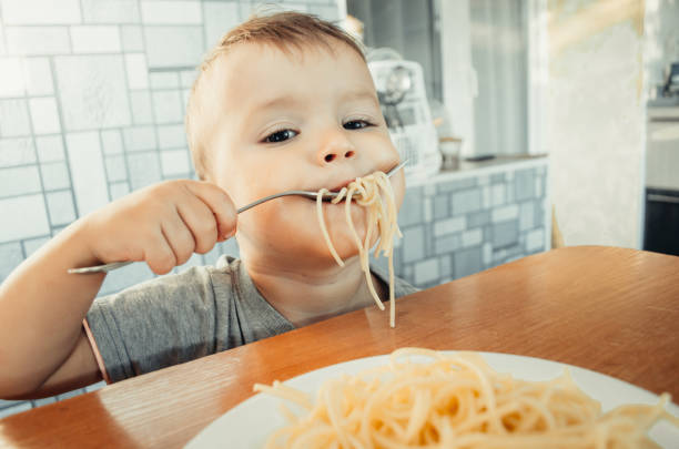 istock Baby in the kitchen eagerly eating pasta 1132002201