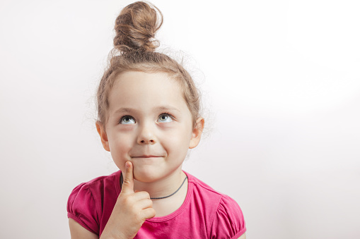 pensive cunning girl looking up and thinking about something. little dreamer in pink T-shirt with finger on lips. kid having a good idea. making up a game