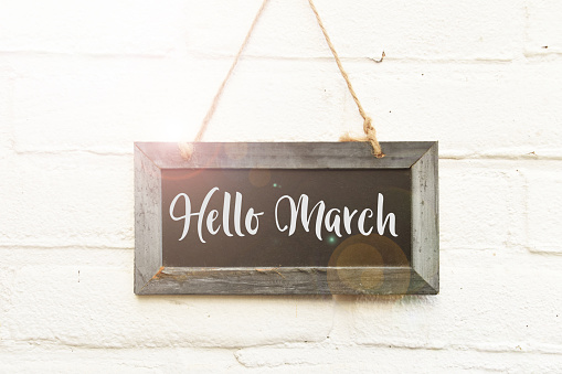 Handwritten text hello March on hanging black chalkboard againt white outdoor wall