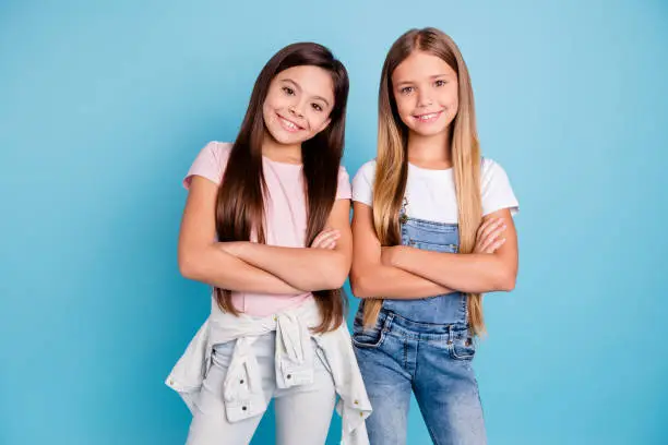 Photo of Portrait of nice-looking cute lovely sweet adorable well-groomed attractive cheerful cheery straight-haired brunette blonde girls siblings folded arms isolated over blue pastel background