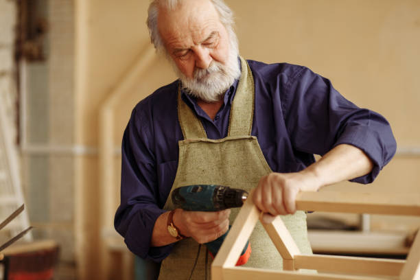 istock old grey headed man is working with drill in the home workshop 1132005838