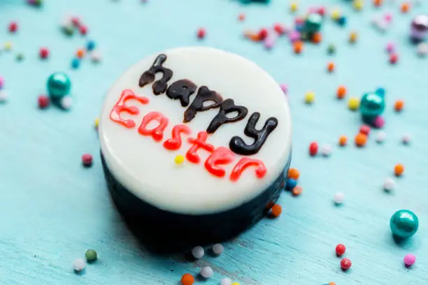 Close up of Happy Easter text on a white chocolate with candies on the wooden table