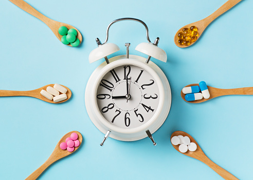 Set of colorful pills and tablets in spoon and alarm clock on blue background. Copy space, top view