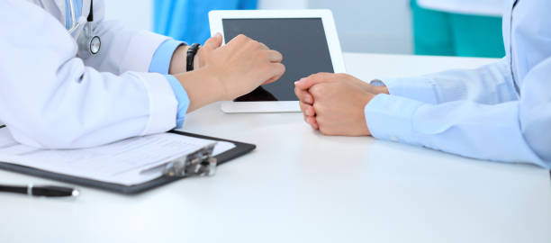 istock Doctor and patient discussing something, just hands at the table, white background. Physician pointing into tablet screen 1132008480