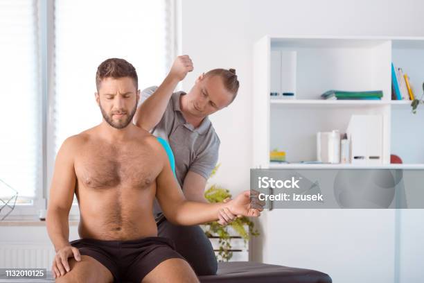 Physiotherapist Massaging Young Man Stock Photo - Download Image Now - Adults Only, Elastic Therapeutic Tape, Massage Therapist