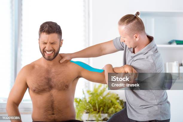 Physiotherapist Stretching Shoulder Of Young Man Stock Photo - Download Image Now - Adhesive Tape, Physical Therapist, Adult