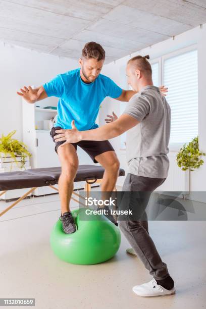 Young Man Excercising On Ball With His Physiotherapist On Ball Stock Photo - Download Image Now