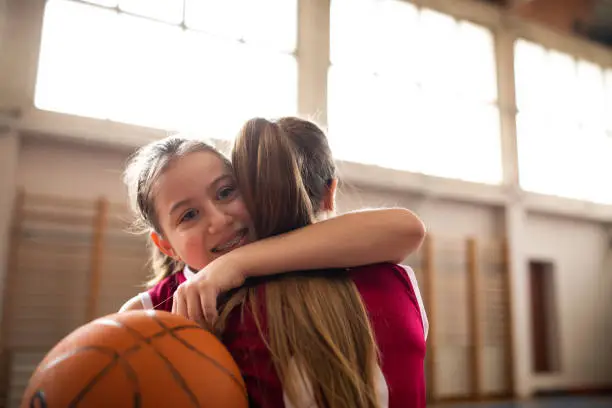 Cute teenage girls, smiling and hugging after basketball match, happy after winning the game