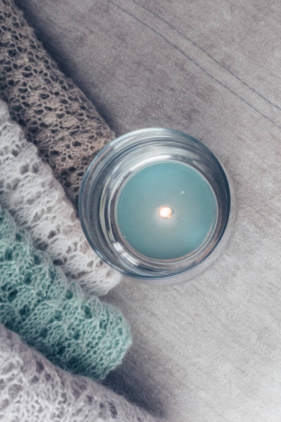 istock Stylish knitted pastel colored sweaters piled on velvety fabric along the lit candle. Top view, copy space. 1132012784