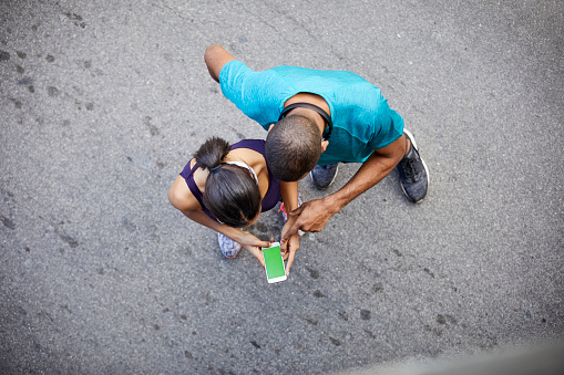 High angle view of couple using mobile phone. Man and woman standing on street. They are in sports clothing.