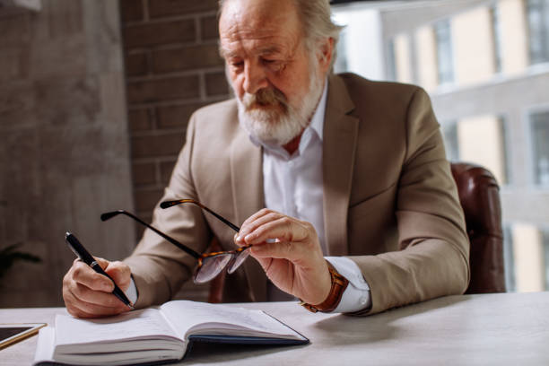 istock old exhausted man is putting his glasses on the desk while making notes 1132017153