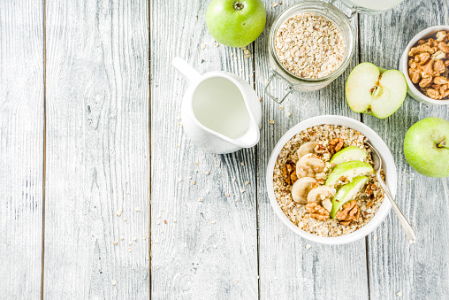 Healthy breakfast oatmeal with nuts ad fruits - apple, banana, walnuts, With milk on wooden background copy space