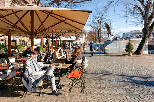 Ljubljana, Slovenia - January 14, 2019: Tourists eating and drinking in restaurants, tables and chairs and Ljubljana old town embankment, Slovenia. People in open air cafes in Slovenian capital city