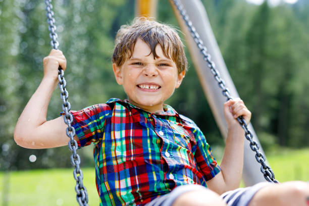 istock Funny kid boy having fun with chain swing on outdoor playground while being wet splashed with water. child swinging on summer day. Active leisure with kids. Happy crying boy with rain drops on face. 1132028059