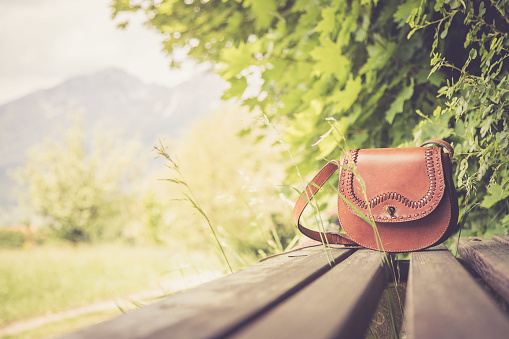 Leather hand bag lies on a wooden park bench, summer time, nobody