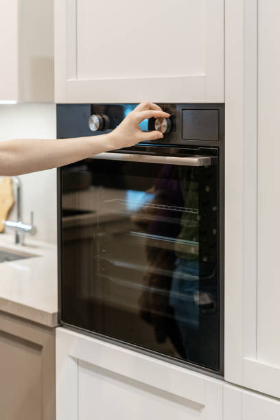 istock Vertical photo of woman hand tuning program on control panel for black built-in oven in white kitchen cabinet 1132032957