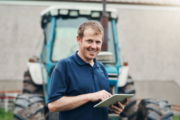 I should put this down at some point Portrait of a cheerful young male farmer browsing on a digital tablet with his tractor in the background put down stock pictures, royalty-free photos & images