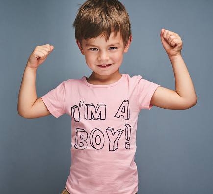 Studio portrait of a cheering boy wearing a shirt with “I’m a boy” printed on it against a grey background