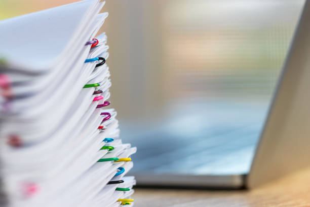 istock Close up stack of paperwork. Pile of unfinished homework assignment stacked in archive with colorful paper clips on wood table waiting to be managed and inspected. Education and business concept. 1132040245