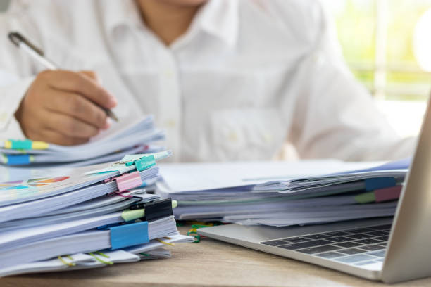 istock Teacher holding pen by hand for checking student homework assignments on desk in school office. Unfinished paperwork stacked in archive with color binder paper clips. Education and business concept. 1132040510