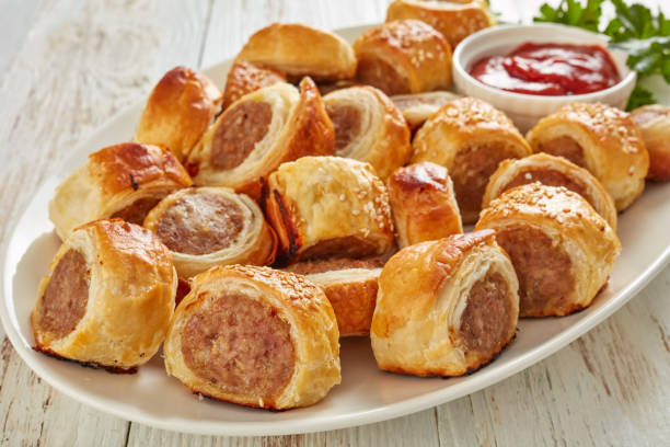 freshly baked Puff pastry Sausage rolls, close-up overhead view of  sausage rolls on a white oval platter with tomato sauce on a wooden rustic table, finger food, english cuisine, view from above, close-up sausage roll stock pictures, royalty-free photos & images