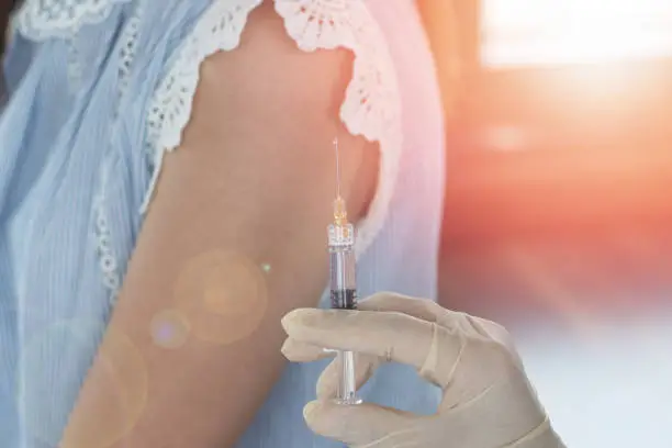 World immunization week and International HPV awareness day concept. Woman having vaccination for influenza or flu shot or HPV prevention with syringe by nurse or medical officer.