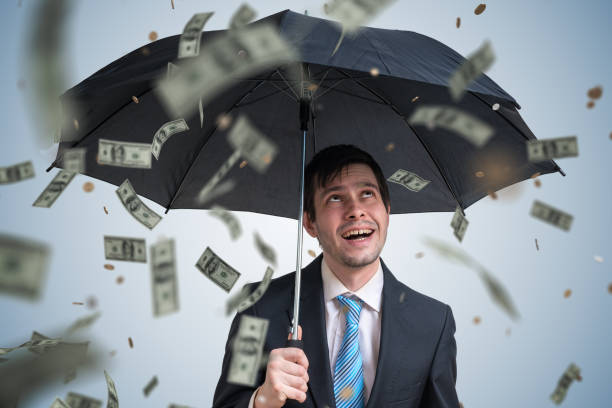 istock Young successful rich businessman with umbrella and money falling down. 1132043952