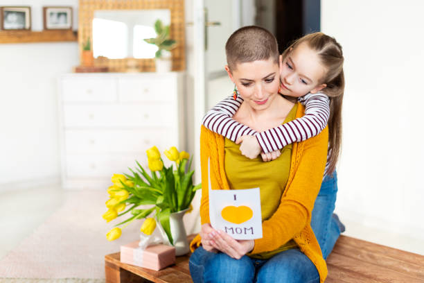 urocza młoda dziewczyna i jej mama, młoda pacjentka na raka, czytająca domową kartkę z życzeniami. koncepcja uroczystości rodzinnych. happy dzień matki lub tło urodzinowe. - mothers day tulip yellow greeting card zdjęcia i obrazy z banku zdjęć