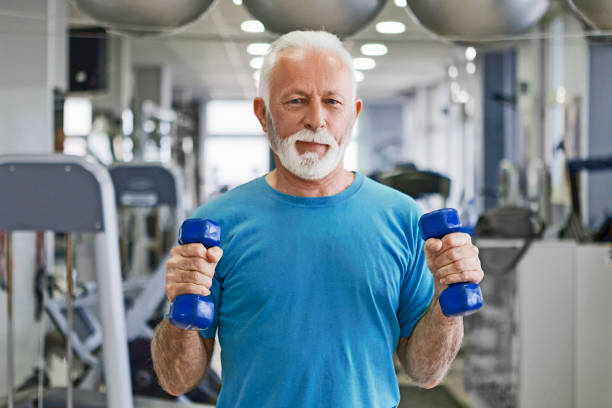 istock Senior man with barbells in gym looking at camera 1132044072