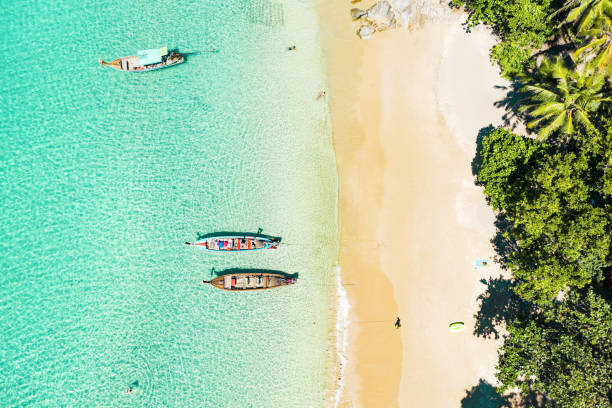 View from above, stunning aerial view of a beautiful tropical beach with white sand and turquoise clear water, longtail boats and people sunbathing, Banana beach, Phuket, Thailand. stock photo