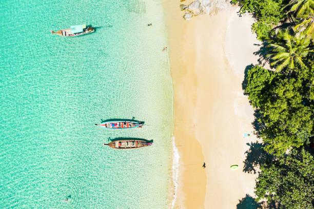 View from above, stunning aerial view of a beautiful tropical beach with white sand and turquoise clear water, longtail boats and people sunbathing, Banana beach, Phuket, Thailand. View from above, stunning aerial view of a beautiful tropical beach with white sand and turquoise clear water, longtail boats and people sunbathing, Banana beach, Phuket, Thailand. bali boat tour stock pictures, royalty-free photos & images