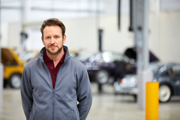Portrait of male engineer in automobile industry Portrait of confident engineer in automobile industry. Male technologist is in showroom. He is wearing jacket while standing in factory. hands behind back stock pictures, royalty-free photos & images