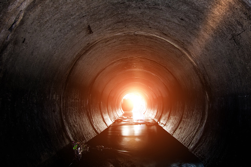 Round underground urban sewer tunnel with dirty sewage water. A light in the end of a tunnel.