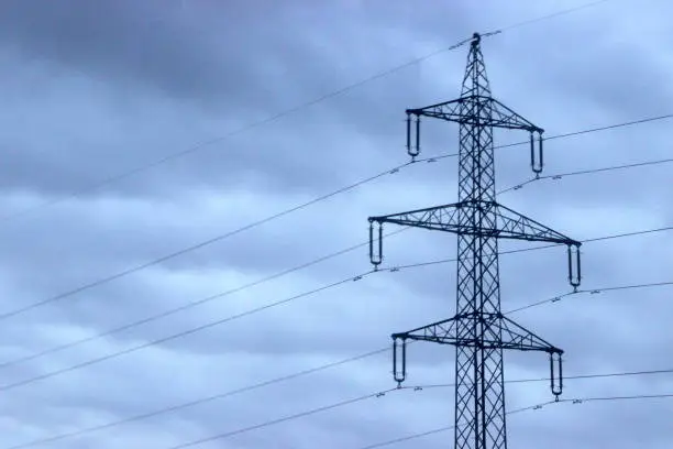upper detail of a high-voltage pylon with a heavily cloudy background