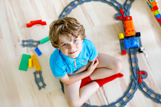 istock Adorable little blond kid boy playing with colorful plastic blocks and creating train station. Child having fun with building railway toys at home 1132047975