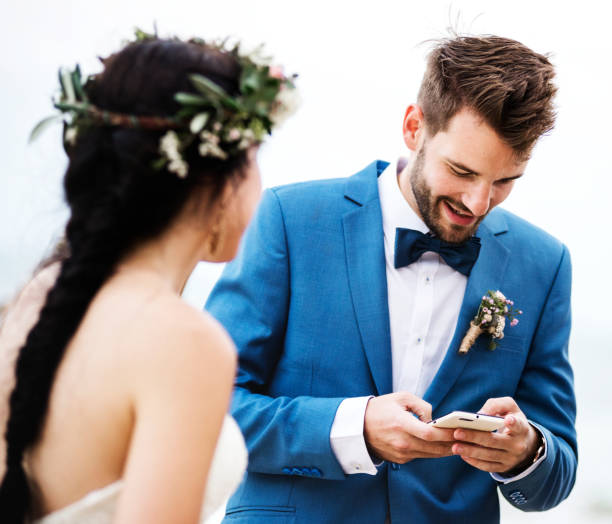 istock Groom checking his phone at beach wedding ceremony 1132049152