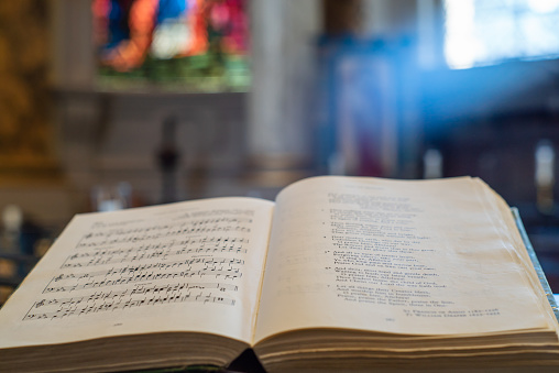 Open hymn book with a stained glass window in the background.
