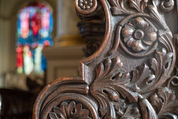 Close up of a carved oak bench end with a stained glass window in the background.
