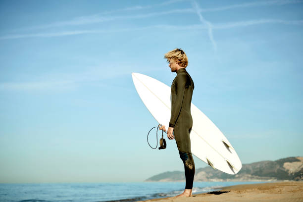 istock Man with surfboard standing on shore at beach 1132054008