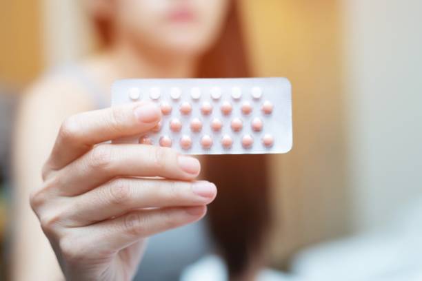 Woman hands opening birth control pills in hand on the bed in the bedroom. Eating Contraceptive Pill. stock photo