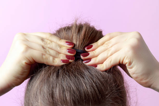 Female hands with red manicure correct the bun. Brown hair. Modern fast hairstyle. Pink background Female hands with red manicure correct the bun. Brown hair. Modern fast hairstyle. Pink background hair band stock pictures, royalty-free photos & images